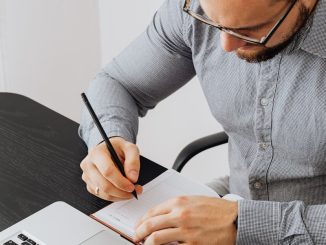 Un homme d'affaires écrit des notes sur un cahier dans un bureau moderne avec un ordinateur portable sur le bureau.